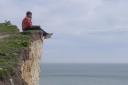 Photographs show a man sitting on the edge of cliffs at Birling Gap