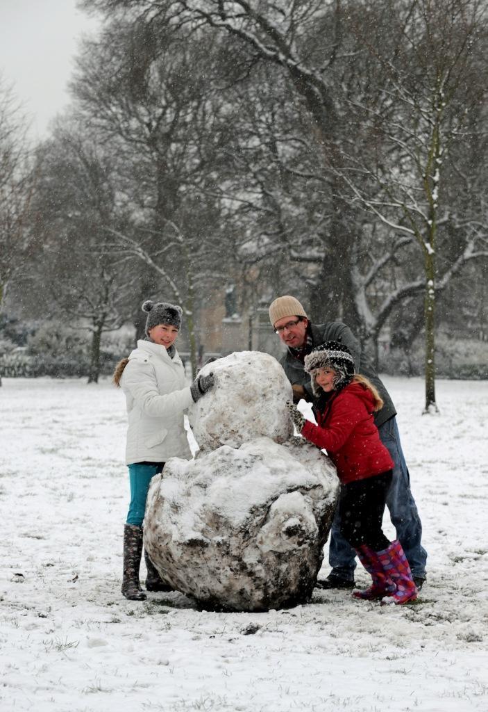 A family enjoy building a snowman in Victoria Gardens as snow begins to fall again in Brighton 