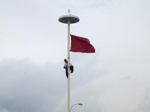 A protester scales a lamp post on the seafront to fly a red flag lamp post