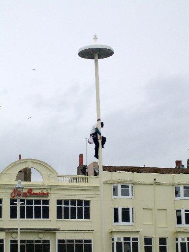 A protester scales a lamp post ready to unfurl a red flag on the seafront. 