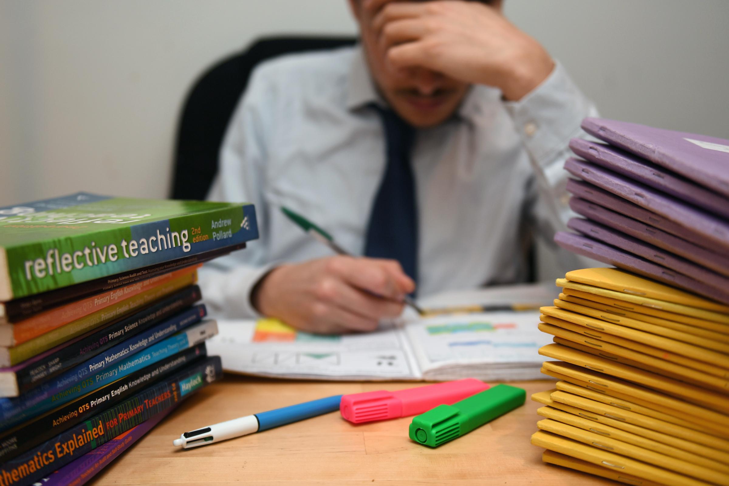 A primary school teacher looking stressed next to piles of classroom books..