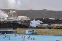 People bathe in the Blue Lagoon as the volcanic crater spews lava in the background in Grindavik, Iceland (Marco di Marco/AP)