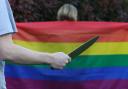A general view of a person holding a knife behind someone wearing an LGBT pride flag.. Stock image.