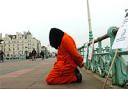 A protester in an orange boiler suit copies the clothing worn by detainees