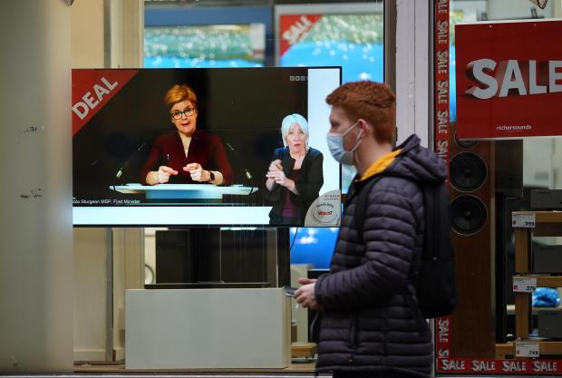 The Argus: Passers-by look at a tv screen in a Glasgow shop showing First Minister Nicola Sturgeon making a Covid-19 statement during a virtual sitting of the Scottish Parliament. Photo taken on December 29, 2021, via PA.