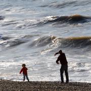 A man and two young boys throw pebbles back into the sea